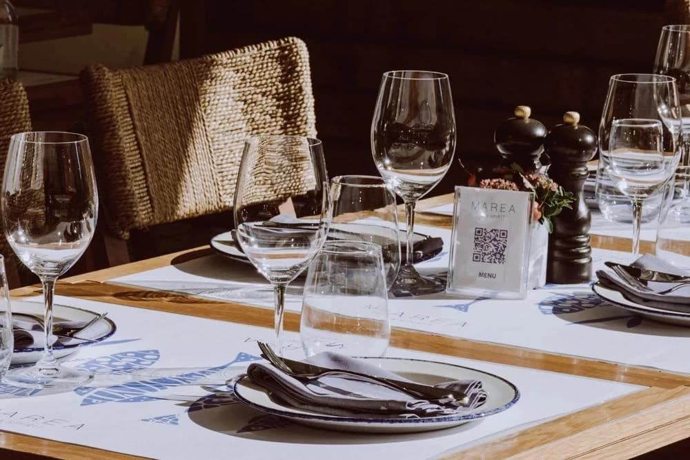 Nakryty stolik restauracji w słońcu: kieliszki, talerze, pieprzniczki i stojak „Menu” z kodem QR